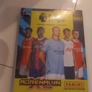Premier League 2023 Adrenalyn XL Collector's Binder - Samlarpärm fylld med officiella Premier League Adrenalyn XL 2023 trading cards från Panini. Perfekt för dig som älskar fotboll, samlar på kort och vill ha en cool och organiserad samling med stjärnspelare och specialkort. Inspirerar till både spel och samlande! Om man köper den kan man byta ut saker och den är full med massor av bra kort men jag har bara 5 bilder att visa produkten. Jag kan också sälja de här korten 1 och 1 om man vill kontakta bara mig om vilka isåfall