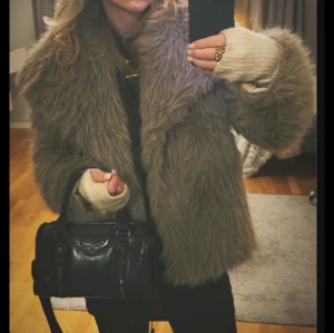 Beige fluffig pälsjacka - Säljer en supermysig och fluffig beige pälsjacka med bred krage och långärmad modell. Jackan har en oversized passform och är perfekt för dig som vill ha en cool och trendig look med extra volym. Materialet är syntetpäls som känns mjuk och varm. Den har ett litet hål inuti men inget som stör funktionen 
