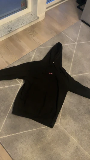  SNUSK hoodie med ryttarmotiv - Svart hoodie från SNUSK med rosa tryck på bröstet och en stor ryttare på häst i rosa på ryggen. Tröjan har huva med snörning och långa ärmar. Perfekt för dig som gillar unika motiv och streetwear-vibe. Storlek XL!!