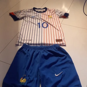 Nike fotbollsställ Frankrike - Säljer ett fotbollsställ Nike med Frankrikes tupp-emblem broderat och Nike-logga. Shortsens midja är elastisk för skön passform och materialet är lätt polyester som andas. Perfekta för dig som älskar fotboll och vill ha en sportig look. Tröja är också bra och elastisk 