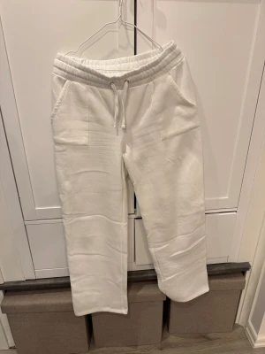 Vita mjukisbyxor från 157, storlek L - Snygga vita mjukisbyxor från 157 i storlek L. De har elastisk midja med snörning, två sidofickor och raka ben. Perfekta för chill dagar eller när du vill ha det extra bekvämt. Materialet är mjukt och skönt bomullstyg.