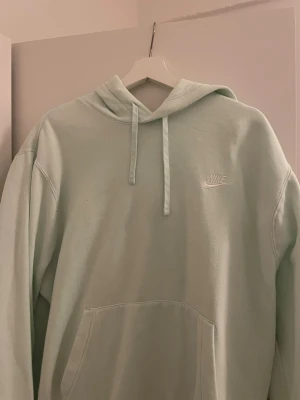 Ljusgrön hoodie från Nike - Snygg ljusgrön hoodie från Nike med klassisk logga broderad på bröstet. Tröjan har huva med snörning och en stor magficka framtill. Perfekt för chill dagar och streetwear-stil. Mjuk bomullskänsla och långärmad modell.