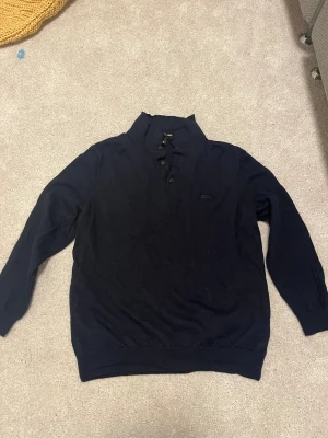 Svart polotröja från BOSS - Svart polotröja från BOSS med diskret broderad logga på bröstet. Tröjan har lång ärm, ribbade muddar och krage med knappar. Tillverkad av finaste italienska garnet för en mjuk och lyxig känsla. Perfekt för dig som gillar stilrena och klassiska plagg.