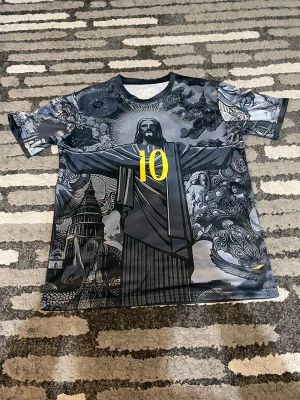 Brasil Neymar Jr #10 fotbollströja - Unik Brasilien fotbollströja med Neymar Jr och nummer 10 i gult på både fram- och baksida. Tröjan har coolt grafiskt mönster med motiv av Kristusstatyn och detaljerade illustrationer i grått och svart. Kortärmad och tillverkad i lätt polyester.