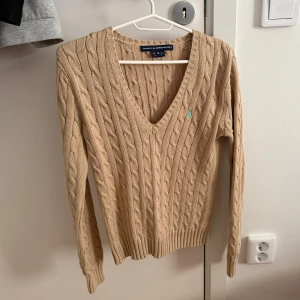 Ralph Lauren Beige stickad tröja - Snygg beige stickad tröja från Ralph Lauren Sport i storlek M men passar S. Tröjan har v-ringning, lång ärm och ett litet blått broderat logomärke på bröstet💞
