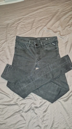 Replay svarta jeans slim fit - Snygga grå jeans från Replay med klassisk femficksdesign och svarta detaljer. Slim fit-modell med raka ben och låg midja. Materialet är mjukt jeans-tyg med stretch för extra komfort. Replay-logga på bakfickan och läderpatch i midjan.