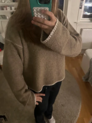 Beige stickad tröja från Kappahl - Mysig beige stickad tröja från Kappahl med lång ärm och loose passform. Tröjan har vita dekorativa sömmar längs ärmar och nederkant som ger en chill vibe. Rund halsringning och mjukt material som passar perfekt för kyliga dagar.