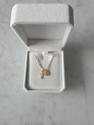 Halsband med kors och medaljong - Snyggt halsband, fyrkantigt länkad kedja. Hänget består av ett litet kors och en oval medaljong med detaljerad yta. Perfekt för dig som gillar stilrena smycken med personlig touch.