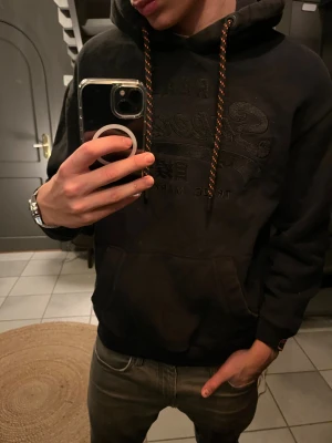 Superdry hoodie   - En svart hoodie från Superdry. Hoodien är tjock och och därför skön att ha på vintern. Sitter bra och har stilren text på. Skriv vid minsta fundering !