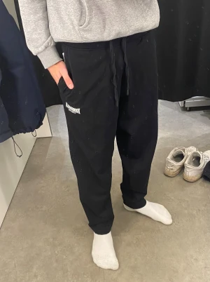 Svarta mjukisbyxor från Lonsdale - Svarta mjukisbyxor från Lonsdale med vit logga på vänster lår. Byxorna har snörning i midjan och en loose passform som ger en chill vibe. Perfekta för att hänga hemma eller dra till gymmet. Mjukt bomullsmaterial och ribbade muddar vid benslut.