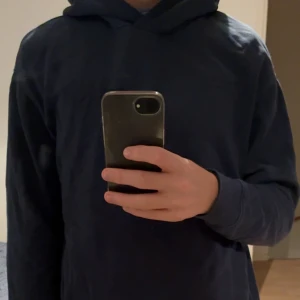 Mörkblå hoodie - Snygg mörkblå hoodie från Röhnisch med broderad logga på ryggen. Tröjan har en stor huva, långa ärmar och är gjord i mjuk bomull. Perfekt för chill dagar och enkel att matcha med jeans eller joggers.