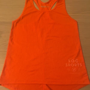 Orange linnetopp från SOC - Sportig orange linnetopp från SOC med meshstruktur och tryck 'SOC SPORTS' framtill. Perfekt för träning med sitt lätta och ventilerande syntetmaterial. Klassisk racerback-modell som ger bra rörelsefrihet.