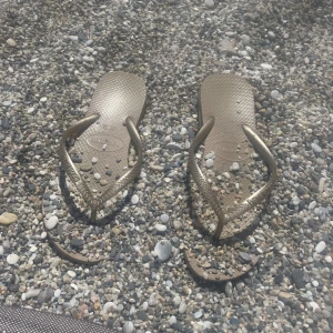 Populära Guldiga flip-flops från Havaianas - Säljer ett par guldiga flip-flops från Havaianas med klassisk design och mönstrade remmar. Perfekta för stranden eller poolen, tillverkade i syntetmaterial som torkar snabbt. Snyggt metallic-look som sticker ut i sommarvärmen.
