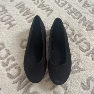 Svarta ballerinaskor i mocka-look - Klassiska svarta ballerinaskor med rund tå och platt sula. Skorna har en stilren design och är tillverkade i ett material som liknar mocka. Perfekta för en enkel och clean stil.