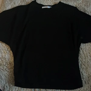 Svart topp från 157 i storlek S - En stilren svart topp från 157 med enkel design och rund hals. Modellen är rak och har korta ärmar, vilket gör den lätt att matcha med olika outfits. Perfekt för dig som gillar minimalistisk stil.
