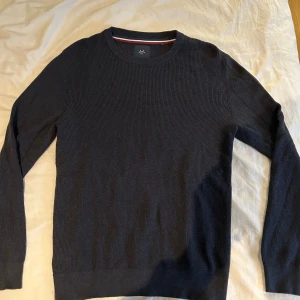 Mörkblå stickad tröja från Lindbergh - Snygg mörkblå stickad tröja från Lindbergh med rund hals och ribbad struktur. Tröjan har långa ärmar och en klassisk passform som funkar till många olika stilar. Perfekt för dig som gillar enkel och stilren design.