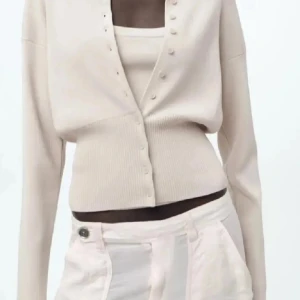 Beige ribbad kofta från Zara - Aldrig använd! Snygg beige kofta från Zara med ribbad nederdel och knappar framtill. Modellen är croppad och har lång ärm, perfekt att styla med ett linne under. Mjuk och stretchig kvalitet som sitter skönt på kroppen.