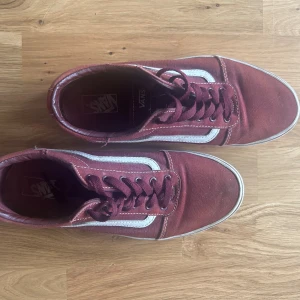Vinröda Vans Old Skool sneakers - Säljer ett par klassiska Vans Old Skool sneakers i vinrött med vit sidorand och vit sula. Skorna har snörning och är tillverkade i canvas med detaljer i syntet. Perfekta för dig som gillar streetstyle och vill ha en ikonisk look.