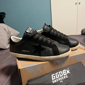 Golden goose - Golden Goose Super-Star sneakers i svart skinn med svart mockadetalj och stjärna på sidan. Klassisk låg modell med snörning och vit platt sula. Insidan är vit och har märkning. Snygg och stilren design med retrovibe. Skick 9,5/10