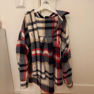 Oversized rutig overshirt i ullmix - Säljer en oversized rutig overshirt med stora blå, röda och beige rutor. Jackan har krage, knappar framtill och långa ärmar. Materialet är en mjuk ullmix som ger en chill och trendig vibe. Perfekt för lager-på-lager och streetstyle.