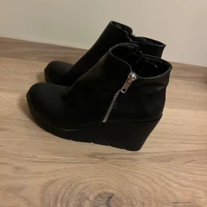 Svarta skor med klack - Säljer ett par svarta stövletter med klack. Dem har en silvrig fakedragkedja och en vanlig svart på insidan. Använda fåtal gånger. Köparen står för frakt 