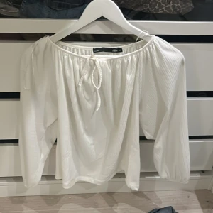 Vit blus med knyt från 157 - TVÄTTAR INNAN JAG SKICKAR OM DU VILL.Säljer en vit blus från 157 i storlek XS. Blusen har ett snyggt knyt framtill vid halsen, offshoulder-design och långa, luftiga ärmar. Materialet är lätt och har en krinklad struktur som ger en cool vibe. Perfekt för dig som gillar romantisk och trendig stil. 