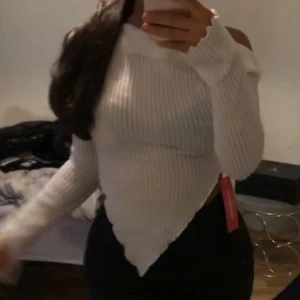 Vit ribbad offshoulder topp - Säljer en vit ribbad topp med offshoulder-design och långärmade ärmar. Toppen har en unik spetsig nederkant framtill som ger en cool och trendig look. Perfekt för dig som gillar att sticka ut med din stil.