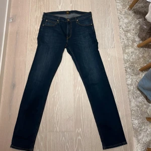 Mörkblå Lee jeans straight fit w34 L34 - Snygga mörkblå jeans från Lee med klassisk straight fit och kontrastsömmar. Modellen har fem fickor, läderpatch med Lee-logga bak och guldfärgade nitar. Jeansen är tillverkade i slitstarkt denim och har normal passform. Mycket fint skick 