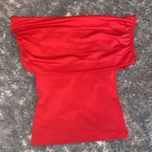 Röd offshoulder tubtopp från H&M Divided - Säljer en snygg röd tubtopp från H&M Divided i storlek XS. Toppen har offshoulder-design med rynkade detaljer upptill och är figurnära. Materialet är mjukt och stretchigt, perfekt för att skapa en cool och trendig look. Den är helt ny och inte använd.