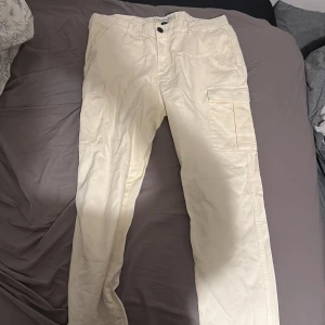 Beiga cargopants med fickor - Säljer ett par beiga cargopants med flera praktiska fickor på sidorna. Byxorna har en rak passform och är tillverkade i slitstarkt bomullsmaterial. Perfekta för dig som gillar funktionella och stilrena byxor.