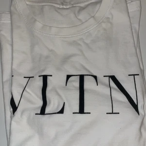 Vit VLTN t-shirt från Valentino - Snygg vit t-shirt från Valentino med VLTN-tryck i svart på bröstet. Klassisk rund hals och korta ärmar. Tillverkad i mjuk bomull som känns skön mot huden. Perfekt för dig som gillar stilrena designer och exklusiva märken.