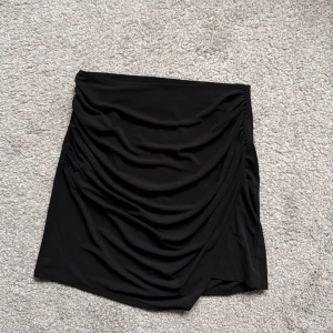 Svart draperad kortkjol - 🤍Svart kortkjol med draperingar och omlottkänsla framtill. Kjolen har en tight passform och är gjord i ett mjukt, stretchigt material 🤍