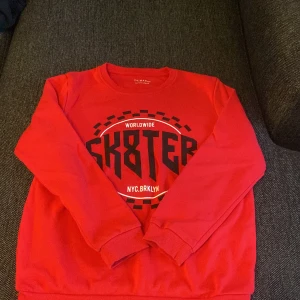 Röd SK8TER sweatshirt - Cool röd sweatshirt från Primark med SK8TER-tryck och NYC.BRKLYN-detaljer framtill. Tröjan har rund hals, långa ärmar och ribbade muddar vid ärmslut och nederkant. Perfekt för dig som gillar streetstyle och skate-vibe.
