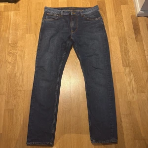 Blå jeans från Nudie Jeans, 32/32 - Säljer ett par klassiska blå jeans från Nudie Jeans i storlek 32/32. Jeansen har raka ben, snygga och Nudie Jeans broderi på bakfickorna. Tillverkade i slitstarkt denim med normal passform och med läderpatch bak. 