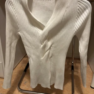 Vit ribbad omlott kofta - Snygg vit ribbad omlott kofta med långärmad design och v-ringad hals. Tröjan har ett twistat omlottparti framtill som ger en cool och modern look. Perfekt att styla med jeans eller kjol för en fräsch vibe.