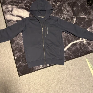 Mörkblå hoodie från Sail Racing L - Mörkblå hoodie från Sail Racing med hel dragkedja och huva. Träjan är i nyskick! Aldrig använt då jag köpte för stor storlek! Den är i storlek L
