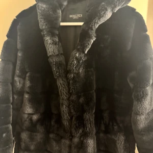 Nyskick topp topp. Svart pälsjacka med stor huva från Hollies - Mer eller mindre oanvänd. Så jag vill tycka nyskick. Men alla tycker olika. Säljer en svart pälsjacka från Hollies med stor fluffig huva och quiltad look. Jackan är riktigt mjuk och fluffig och stor go luva. Har en lyxig känsla som man har med en Hollies (nypris i butik ca 2500kr,) perfekt för dig som vill ha en håll babblan statement piece. Fodrad insida och långärmad modell. Snygg och varm för kalla dagar. Man känner sig lyxig. Men jag försvann i den… vilket är otroligt tråkigt… 