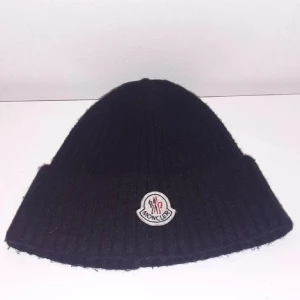 Svart äkta moncler mössa - Svart ribbstickad mössa från Moncler med klassisk logotyp framtill. Sälj på grund av ingen användning. Mycket bra skick till bra skick. 