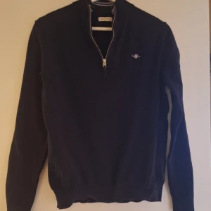 Mörkblå GANT tröja med half zip - Snygg mörkblå tröja från GANT med half zip och liten broderad logga på bröstet. Tröjan har långärmad passform och är tillverkad i mjuk bomull. Perfekt för dig som gillar klassisk stil med en modern touch.