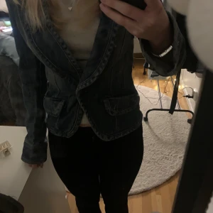 Figursydd jeans jacka  - Säljer en snygg mörk jeansjacka med klassisk krage och två framfickor. Jackan har markerade sömmar och knäppning framtill, perfekt för dig som gillar en cool och stilren look. Passar dig som vill ha en kavaj med lite edge.