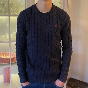 Mörkblå kabelstickad tröja från Morris - S - Jag säljer den här riktigt snygga kabelstickade tröjan från Morris i storlek S. Den är använd men fortfarande i fint skick utan skador och hål. Det enda är att etiketten i nacken sitter lite löst. Nypris ligger på 1699kr och jag säljer den här för 449kr. Tveka inte att höra av er!