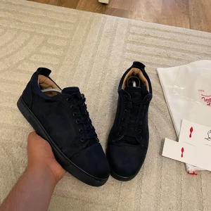 Mörkblå sneakers från Christian Louboutin - Snygga mörkblå sneakers från Christian Louboutin i mocka med svart platt sula och ton-i-ton broderad logga på hälen. Skorna har klassisk snörning och en stilren, minimalistisk design som passar perfekt till jeans eller dressade byxor.storlek 43 passar 42 kvitto finns