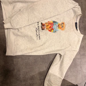 Grå sweatshirt Polo Ralph Lauren L - Säljer en grå sweatshirt från Polo Ralph Lauren i storlek L men passar även M. Rund hals och långa ärmar, mjukt material som är skönt mot huden, passar perfekt med en overshirt över🤩