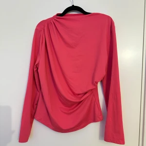 Rosa långärmad topp från SHEIN - Säljer en snygg rosa långärmad topp från SHEIN i storlek XL. Toppen har draperade detaljer vid axeln och sidan som ger en cool och modern look. Materialet är mjukt och stretchigt polyester, perfekt för dig som gillar färg och stil.