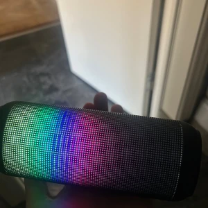 Bluetooth LED-högtalare - Portabel Bluetooth-högtalare med färgglad LED-belysning. Perfekt för fester och utomhusbruk. Högtalaren ser ut att vara i gott skick utan synligt slitage eller defekter. Ger bra ljud och har en modern design med ljuseffekter.