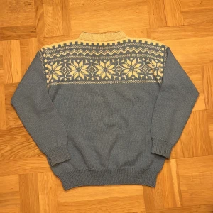 Blå stickad tröja med mönster - Säljer en blå stickad tröja med krage och snyggt vitt mönster över axlar och bröst. Skulle säga att det är storlek medium. 65 i längd, 55 i bredd