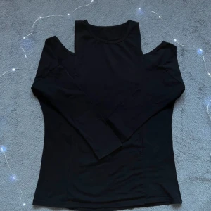 Svart långärmad topp med cut-outs - Snygg svart långärmad topp med coola cut-outs vid axlarna som ger en offshoulder-vibe. Mjuk och stretchig, perfekt att styla med jeans eller kjol. Enkel design med rund hals och figurnära passform.