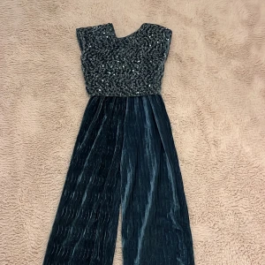 Glittrig långklänning i sammet - Supersnygg långklänning med glittrig paljettöverdel och plisserad sammetskjol i mörkblått. Klänningen har korta ärmar och en elegant, figurnära passform upptill. Perfekt för dig som vill sticka ut med både glamour och stil.