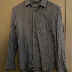 Ljusblå linneskjorta med ficka - Snygg ljusblå skjorta i linne med klassisk krage och bröstficka. Skjortan har långa ärmar och knäppning framtill, perfekt för en chill och stilren look. Luftigt material som passar bra till varmare dagar.