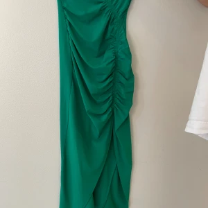 Grön långklänning från Self-Portrait - Snygg grön långklänning från Self-Portrait med draperade detaljer längs framsidan som ger en cool och modern look. Klänningen har en figurnära passform och är tillverkad i ett mjukt syntetmaterial som faller fint. Perfekt för dig som vill sticka ut.